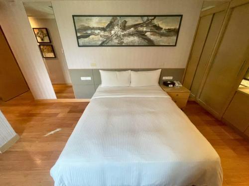 a large white bed in a room with a painting at Delton Hotel in Kaohsiung