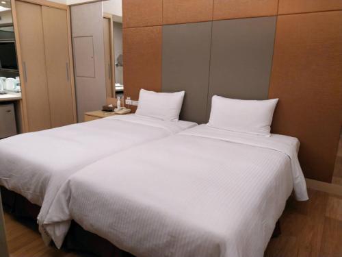 two beds in a hotel room with white sheets at Delton Hotel in Kaohsiung