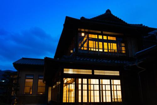 an asian building with illuminated windows at dusk at Yamada Bessou くつろぎの温泉宿 山田別荘 in Beppu