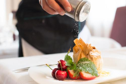 a person is sprinkling food on a plate of food at Kreativ Hotel Landhaus Schweigl in Ultimo