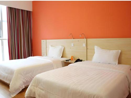 two beds in a hotel room with orange walls at 7 Days Inn Chengdu Huayang Metro Station Binfen Plaza in Chengdu