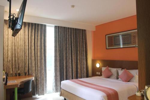 a hotel room with a bed and a desk and a window at Pomelotel Patra Kuningan Jakarta in Jakarta
