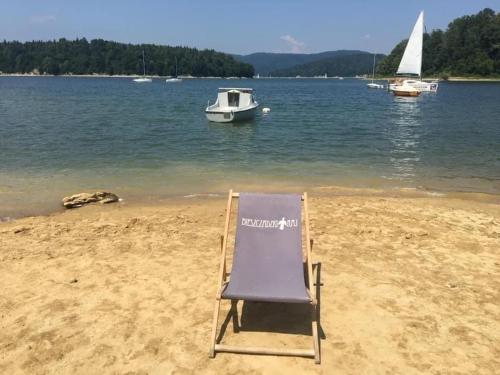 a chair on a beach with a boat in the water at BIESZCZADZKI RAJ Komfortowe domy z kominkami i Sauną na obiekcie in Olchowiec