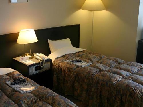a hotel room with two beds with a lamp and a phone at Alpha Hotel Tokushima in Tokushima