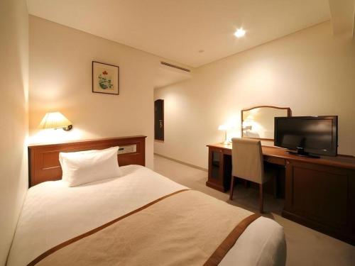 a hotel room with a bed and a desk with a television at Hotel Harvest In Yonago in Yonago