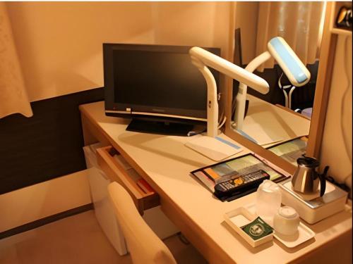 a desk with a computer monitor and a lamp on it at Isehara Green Palace Hotel in Isehara