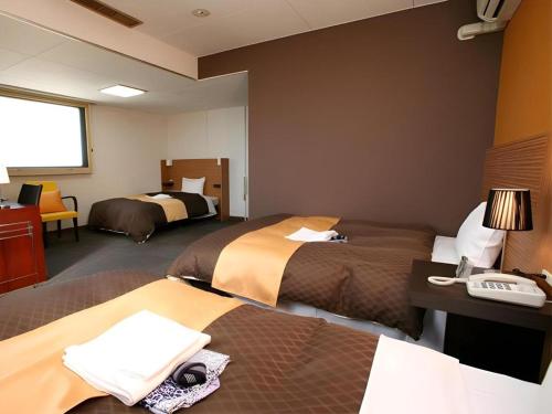 a hotel room with two beds and a desk at Hotel 1-2-3 Kofu Shingen Onsen in Kofu