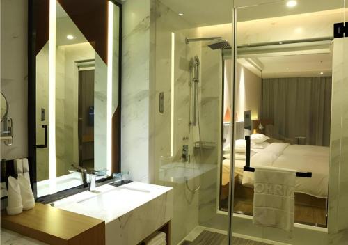 ein Badezimmer mit Waschbecken und Dusche und ein Bett in der Unterkunft Borrman Hotel Hechi Bama Central Cultural Plaza in Bama