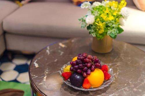 a bowl of fruit on a glass table with a vase of flowers at Huafa Executive Apartment Hotel Zhuhai in Zhuhai