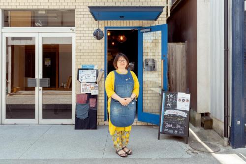a woman is standing in front of a building at Denim Lodge Nest in Kurashiki