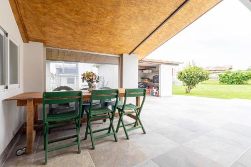 Un patio con una mesa de madera y sillas verdes. en Villa Soto de la Marina I Playas I Jardines, en Santa Cruz de Bezana