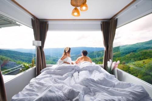 a couple sitting in bed in front of a window at ชิวชิวแคมป์ ภูชี้ฟ้า in Ban Huai Han