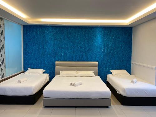 two beds in a room with a blue wall at Codidik Hotel in Kuantan