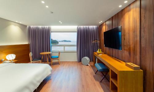 a hotel room with a bed and a desk with a television at Am Ort Hotel in Yeosu