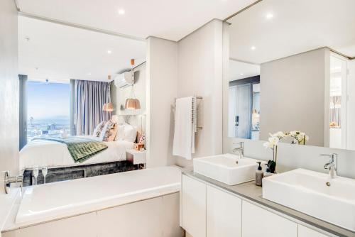 a white bathroom with two sinks and a bed at Luxury 2BR Sky Suite City Views & Prime Location in Cape Town