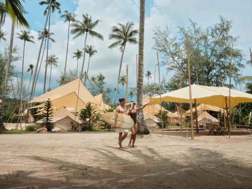 a man walking on the beach with a surfboard at The Survival by Seudam in Ko Kood
