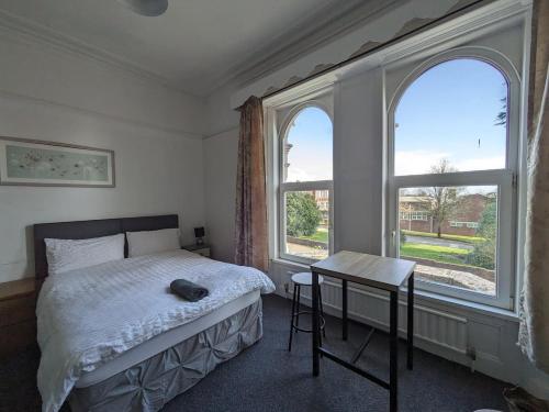 a bedroom with a bed and a table and two windows at Ensuite triple room by Swansea University Hospital v in Swansea