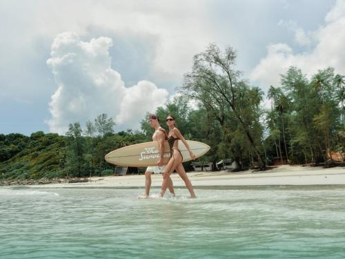 two women walking in the water with a surfboard at The Survival by Seudam in Ko Kood