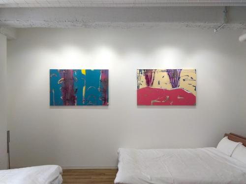 three paintings hanging on a wall above two beds at 肴町街舎 in Hamamatsu