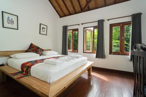 a bedroom with a bed with white sheets and windows at Tricky Trees Lodges in Gili Air