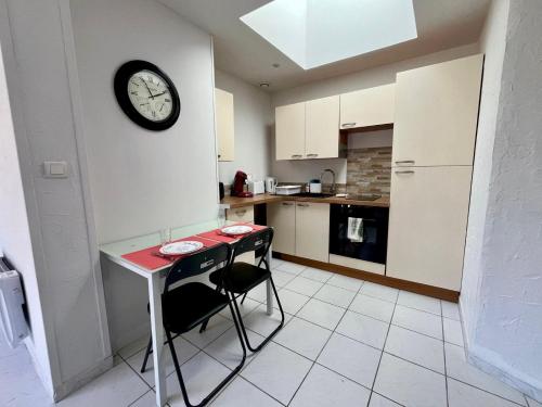 une cuisine avec une table et une horloge au mur dans l'établissement Maisonnette, à 50m de la mer avec terrasse, à Luc-sur-Mer