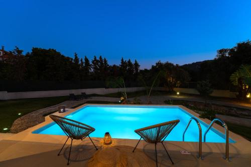 a swimming pool at night with two chairs next to it at SunnyVilla Rhodes in Ialysos
