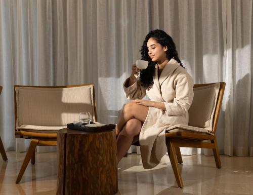 a woman sitting in a chair holding a cup of coffee at Idou Malabata Beach and SPA in Tangier