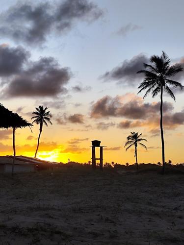 a sunset on the beach with palm trees and a monument at Charmoso Village no Povoado de Coqueiros in Jandaíra