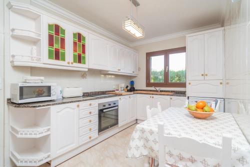 a kitchen with white cabinets and a table with a bowl of fruit at Can Joan in Cala Figuera