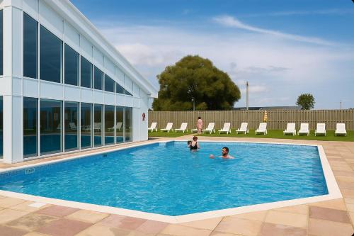 two people swimming in a swimming pool next to a building at Rohannah A&C Ultimate Caravan Retreat in East Mersea