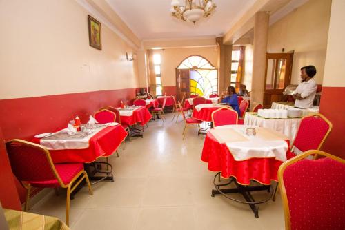 een restaurant met rode tafels en stoelen en een staande man bij Silver Bells Hotel in Isiolo