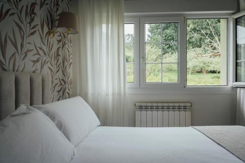 a bedroom with a white bed and two windows at Hotel San Jorge in Nueva de Llanes