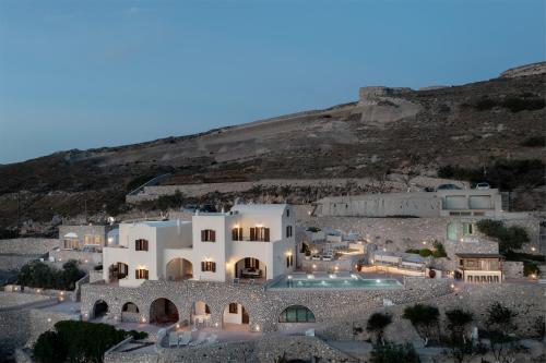 a large white building with a hill in the background at Zatrikion Santorini Villas in Pirgos