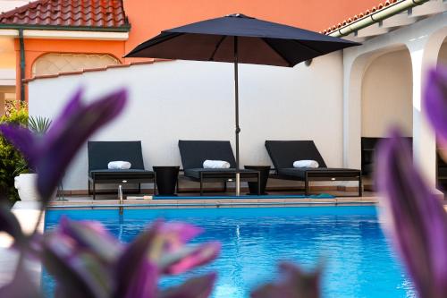 a pool with chairs and an umbrella and purple flowers at Casa Bianca in Barbat na Rabu