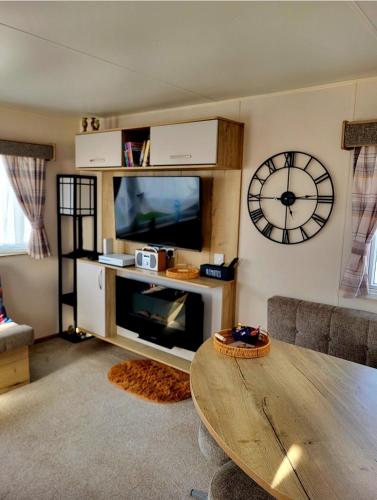 a living room with a table and a clock on the wall at 61 St Andrew's 3 bedroom Cozy Caravan near Edinburgh Seton Sands Holiday Village in Port Seton
