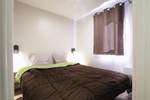 a bedroom with a bed with a brown comforter and a window at Camping Le Florenville in Florenville