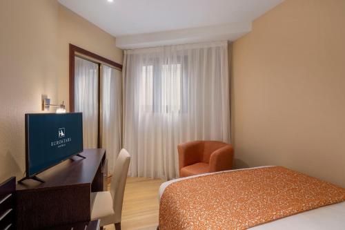 a hotel room with a bed and a television and a chair at Eurostars Plaza Acueducto in Segovia