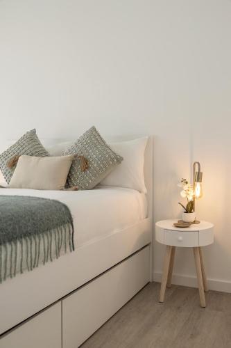 a white bedroom with a bed with a side table at Consolação Surf & Pool Terrace in Atouguia da Baleia
