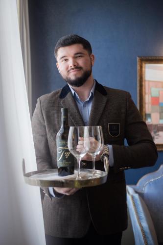 a man holding a tray with a bottle of wine and glasses at Balthazar Design Hotel in Kraków
