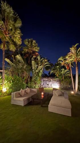 two couches in a yard with palm trees at night at Kudus Boutique Hotel in Canggu 100m to Beach in Canggu