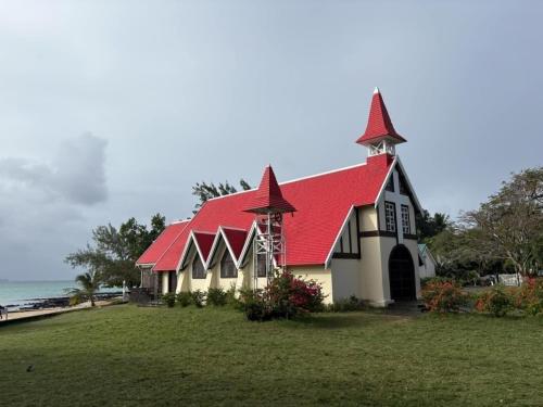 a church with a red roof and the ocean at Appartement résidence des Camélias Ile Maurice in Flic-en-Flac
