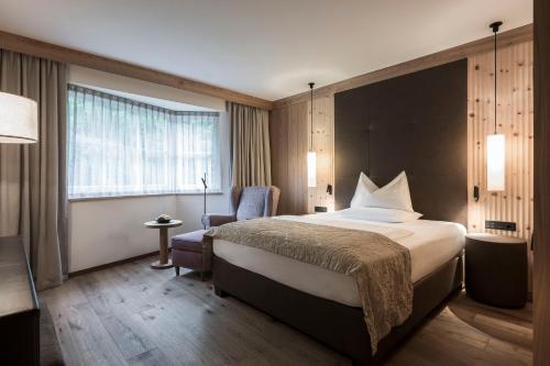 a hotel room with a large bed and a chair at Adler Spa Resort Dolomiti in Ortisei