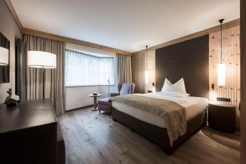 a hotel room with a large bed and a chair at Adler Spa Resort Dolomiti in Ortisei