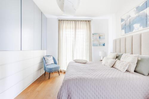 a white bedroom with a bed and a blue chair at The Secret Escape Villa in Sant' Alessio