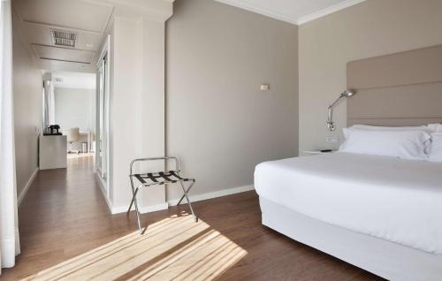 a white bedroom with a white bed and a chair at NH Las Palmas Playa las Canteras in Las Palmas de Gran Canaria