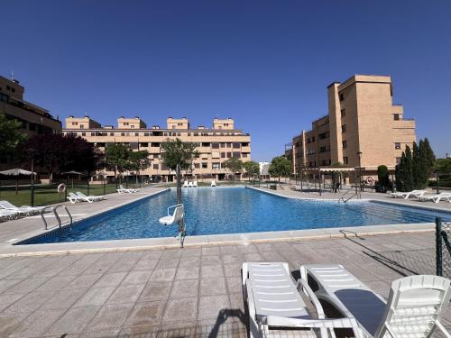 a large swimming pool with white chairs and buildings at Apartamento cerca Universidad de Albacete in Albacete