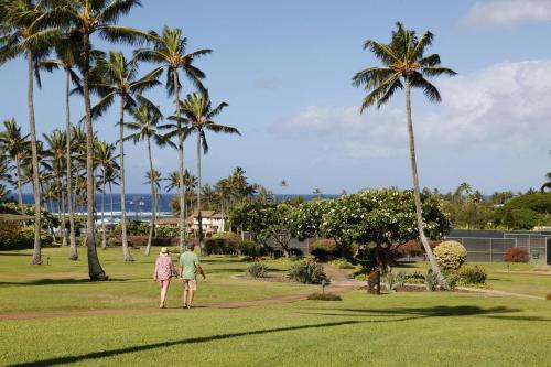 a man and woman walking through a park with palm trees at Hiki Moe Hale by Gather: Elegant 4BR Oasis w/ Pool & Hot Tub in Koloa