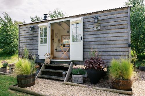 a tiny house with white doors and potted plants at Herbie's Shepherd's Hut - Wellness & Hot Tub in Bottesford