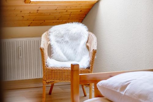 a white cat sitting in a wicker chair next to a bed at Ferienwohnung Veronika Heilbock in Sankt Peter