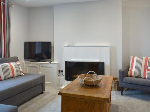ein Wohnzimmer mit einer Couch, einem Tisch und einem Fernseher in der Unterkunft Coastguard Cottage in Ryde